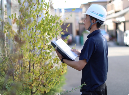 住宅の外観を確認しながら点検記録を取る施工管理担当者
